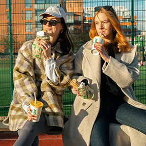 to kvinder sidder på bænk og drikker sodavand og spiser subs fra Subway