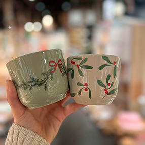 Kopperne bliver holdt fremme i butikken. Der ses en kop med gran og en kop med mistelten motiv